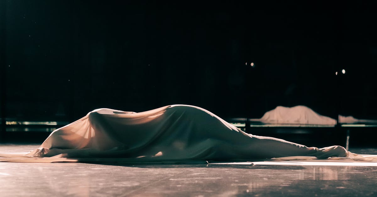 A draped figure in shadow, cloth falling in long dark folds toward gold light