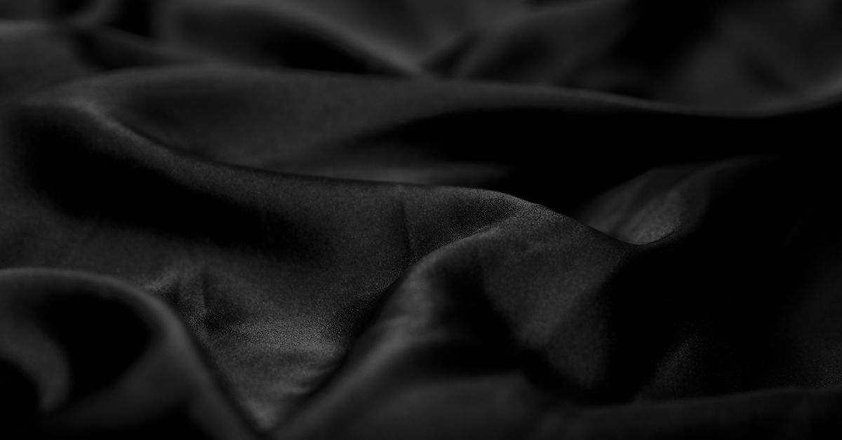 Folds of dark luxury fabric catching low gold light against a black backdrop