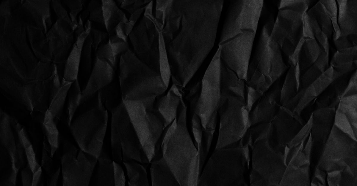 Torn discarded fabric scraps piled in shadow under harsh low light