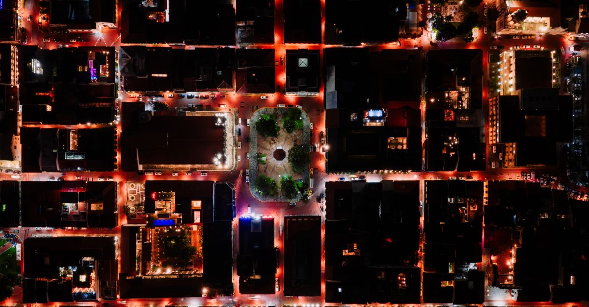 Aerial view of a dark city at night, its grid of lights forming a web of connections